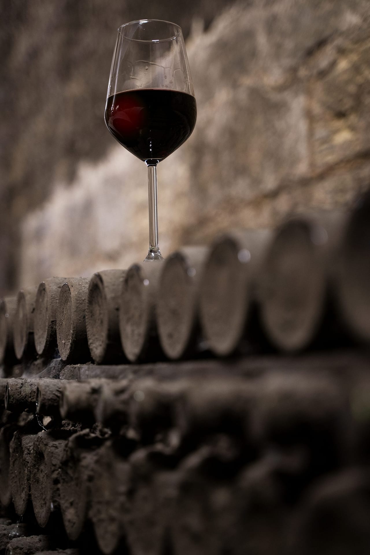 glass with red wine on aged wine bottles in vintage wine cellar